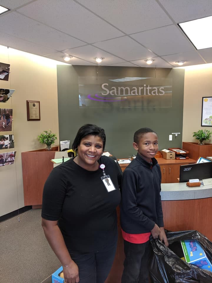 Smiling woman and boy stand with donation bags in front of a Samaritas reception desk.