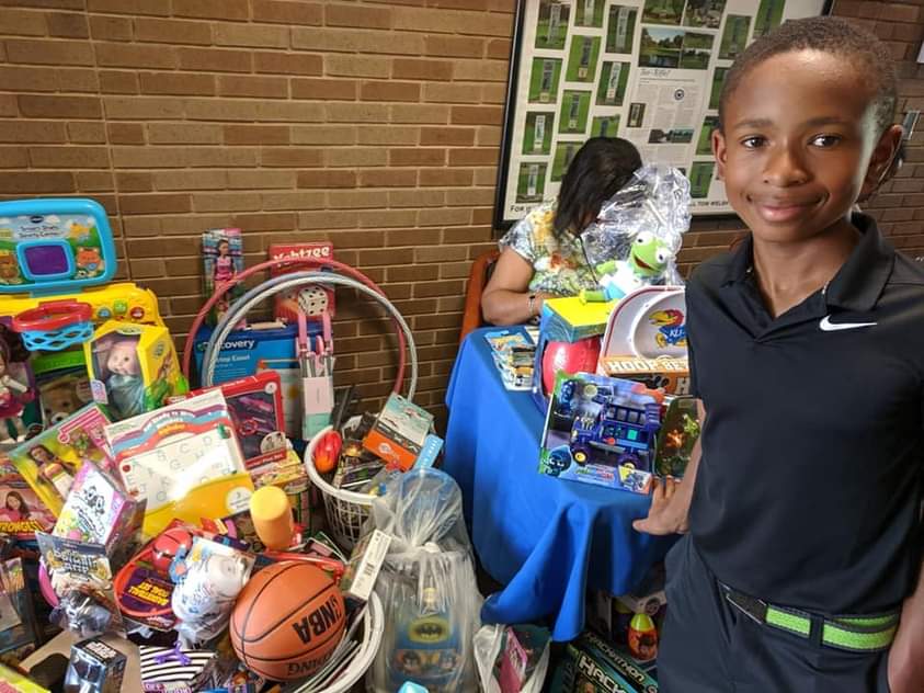 Smiling young boy stands next to a large donation of toys, games, and sports equipment.